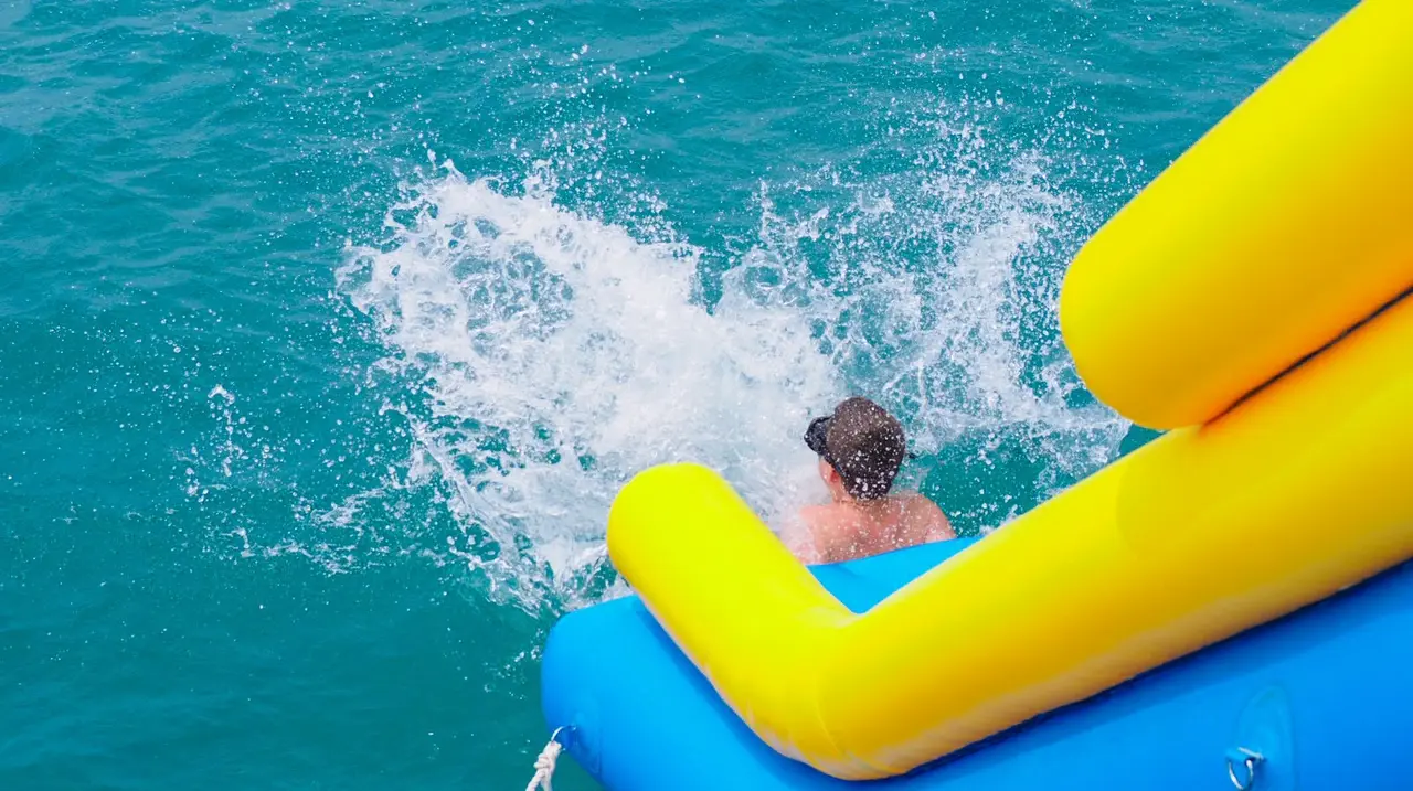 A guest splashing into the sea at the bottom of a yacht’s water slide
