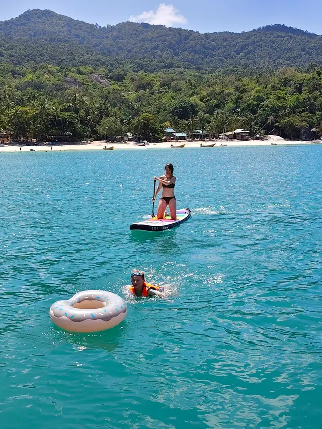 A guest on a paddle board and a float in turquoise water off a beach