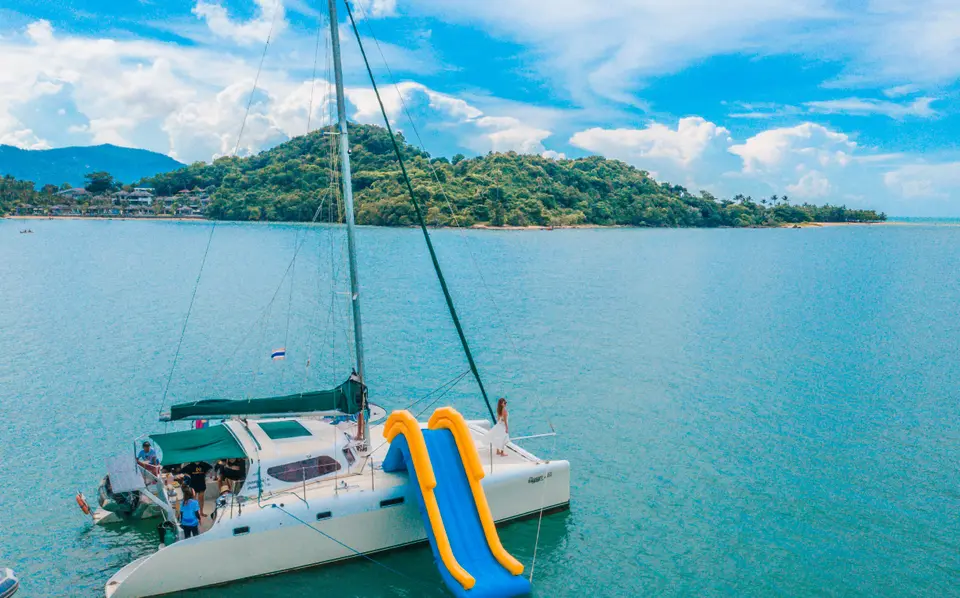 Nina, a 15-guest sailing catamaran yacht, at anchor in turquoise water with her water slide out