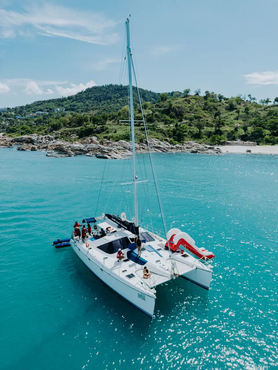 Scarlet, a 20-guest Privilege 43 sailing catamaran yacht, at anchor in turquoise water below a green headland