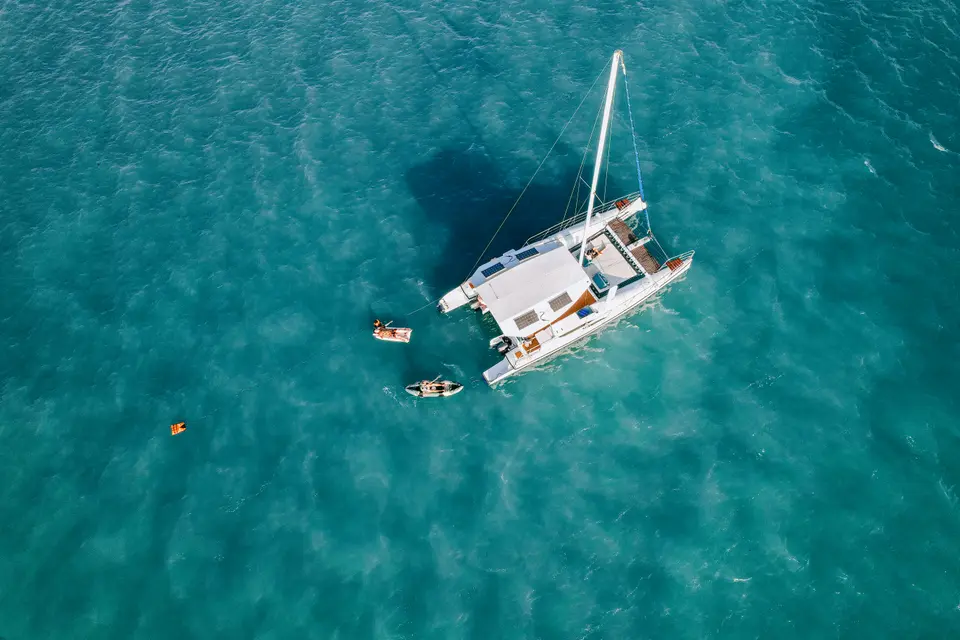 Victoria, a 13-guest private charter yacht, at anchor in turquoise water with guests swimming, seen from above