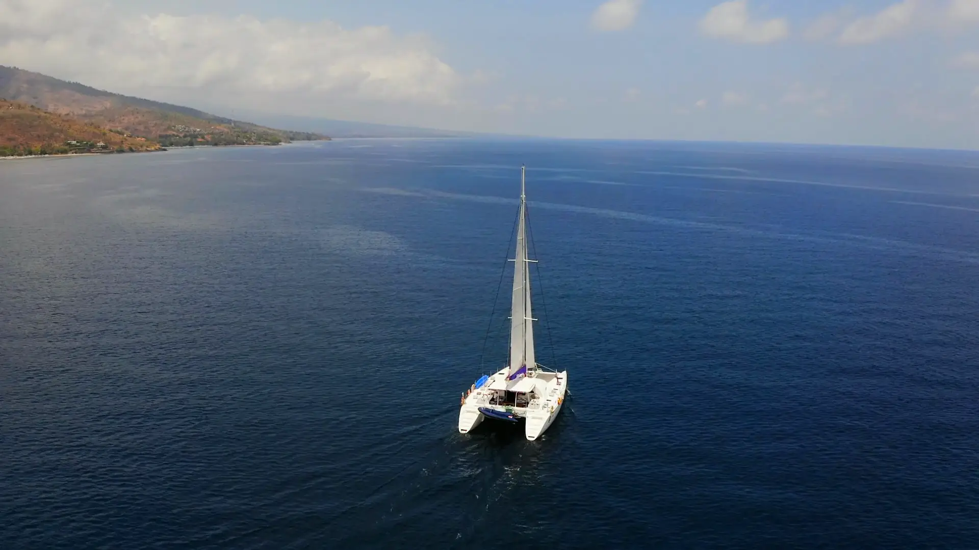 A private sailing catamaran yacht under full sail on deep blue water off a tropical coast